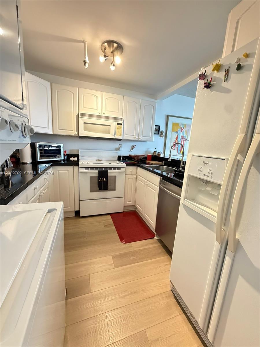 A galley-style kitchen features white cabinets, stainless steel appliances, and light wood-look flooring — 540 Brickell Key Dr # 828, Miami FL 33131, MIAMI, FL