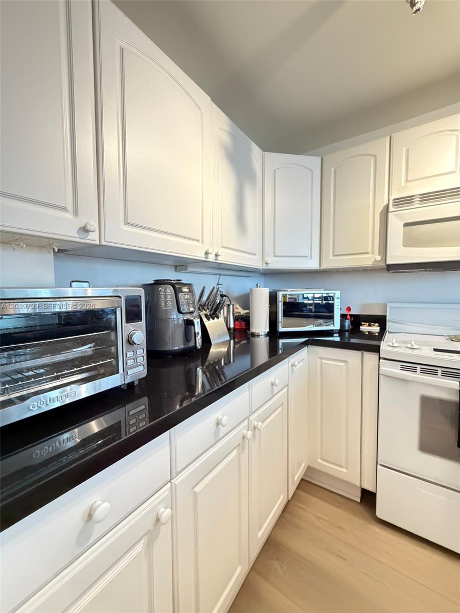 A kitchen features white cabinets, black countertops, and stainless steel appliances — 540 Brickell Key Dr # 828, Miami FL 33131, MIAMI, FL