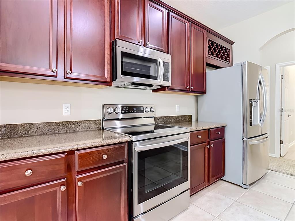 A kitchen features dark wood cabinets, stainless steel appliances, and speckled granite countertops — 3603 DAYDREAM PLACE, ST CLOUD, FL