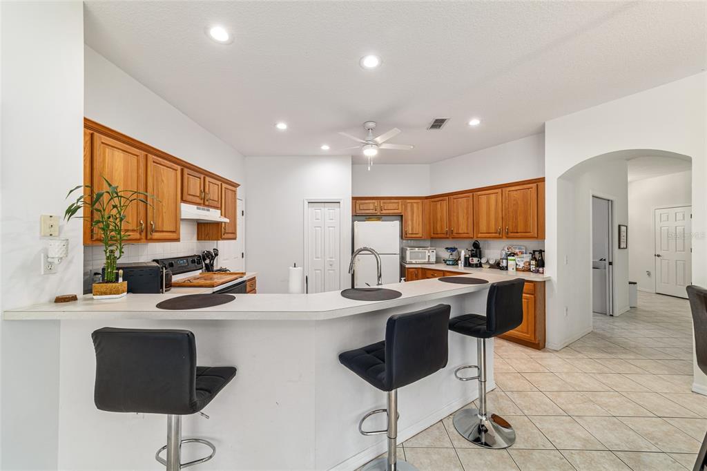 A kitchen with oak cabinets, white countertops, a breakfast bar, and two black bar stools — 20870 SW 90TH LOOP, DUNNELLON, FL