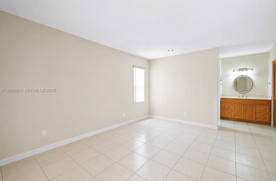 An empty bedroom features beige walls, light-colored tile flooring, a window, and an attached bathroom — 13440 SW 28th St, Miami FL 33175, MIAMI, FL