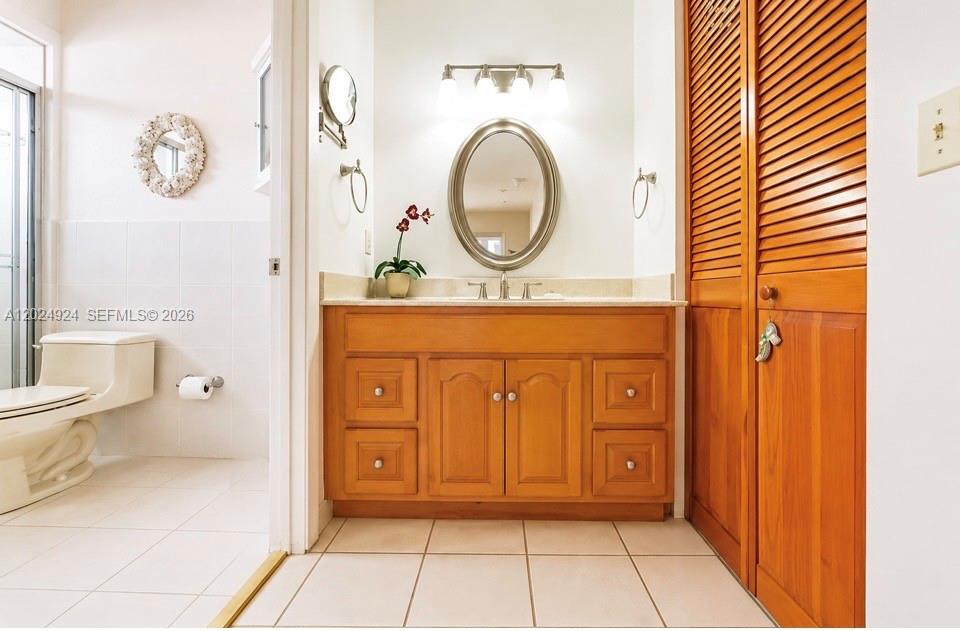 A bathroom features a wooden vanity, an oval mirror, a toilet, and louvered closet doors — 13440 SW 28th St, Miami FL 33175, MIAMI, FL