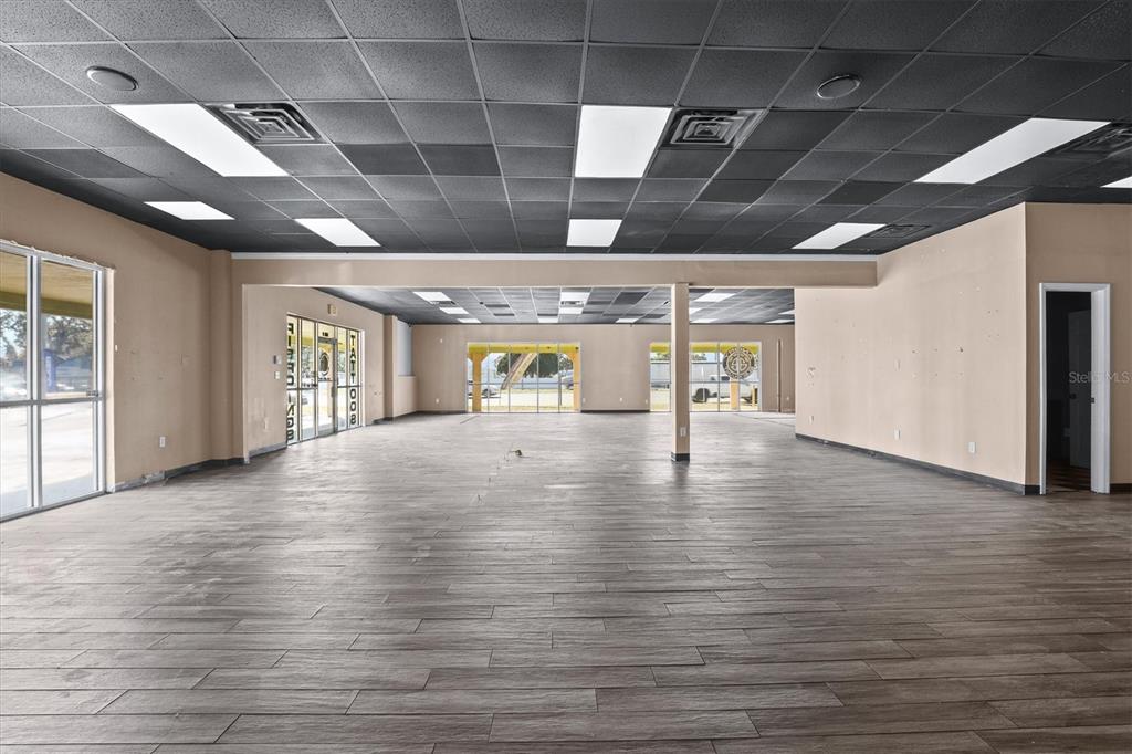 An empty commercial space features wood-look tile flooring, tan walls, and a black drop ceiling — 102 PIERCE CHRISTIE DRIVE, VALRICO, FL