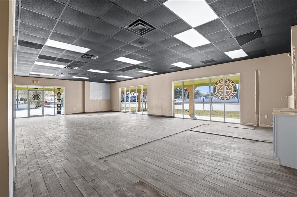 An empty commercial space features wood-look tile flooring, a black drop ceiling, and large windows — 102 PIERCE CHRISTIE DRIVE, VALRICO, FL