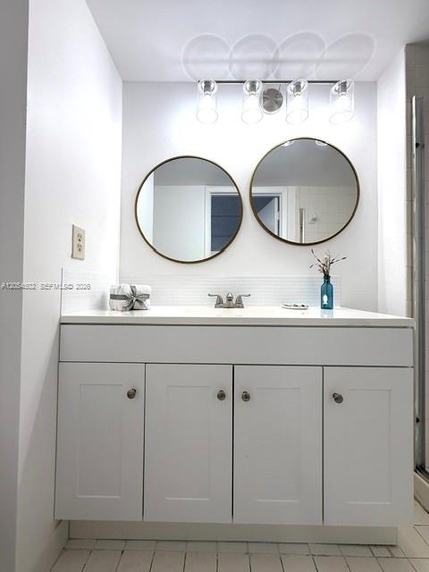 A bathroom vanity with white cabinets, a white countertop, two round mirrors, and overhead lighting — 871 NE 207th Ter # 102, Miami FL 33179, MIAMI, FL