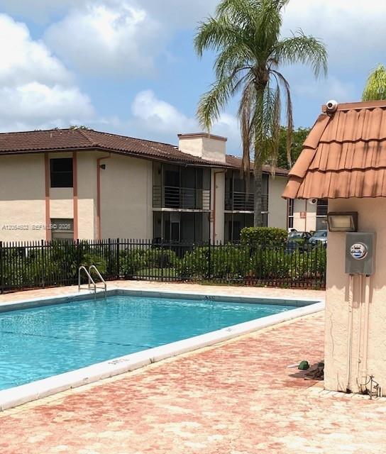 A swimming pool sits in front of a multi-story apartment building with a palm tree — 871 NE 207th Ter # 102, Miami FL 33179, MIAMI, FL
