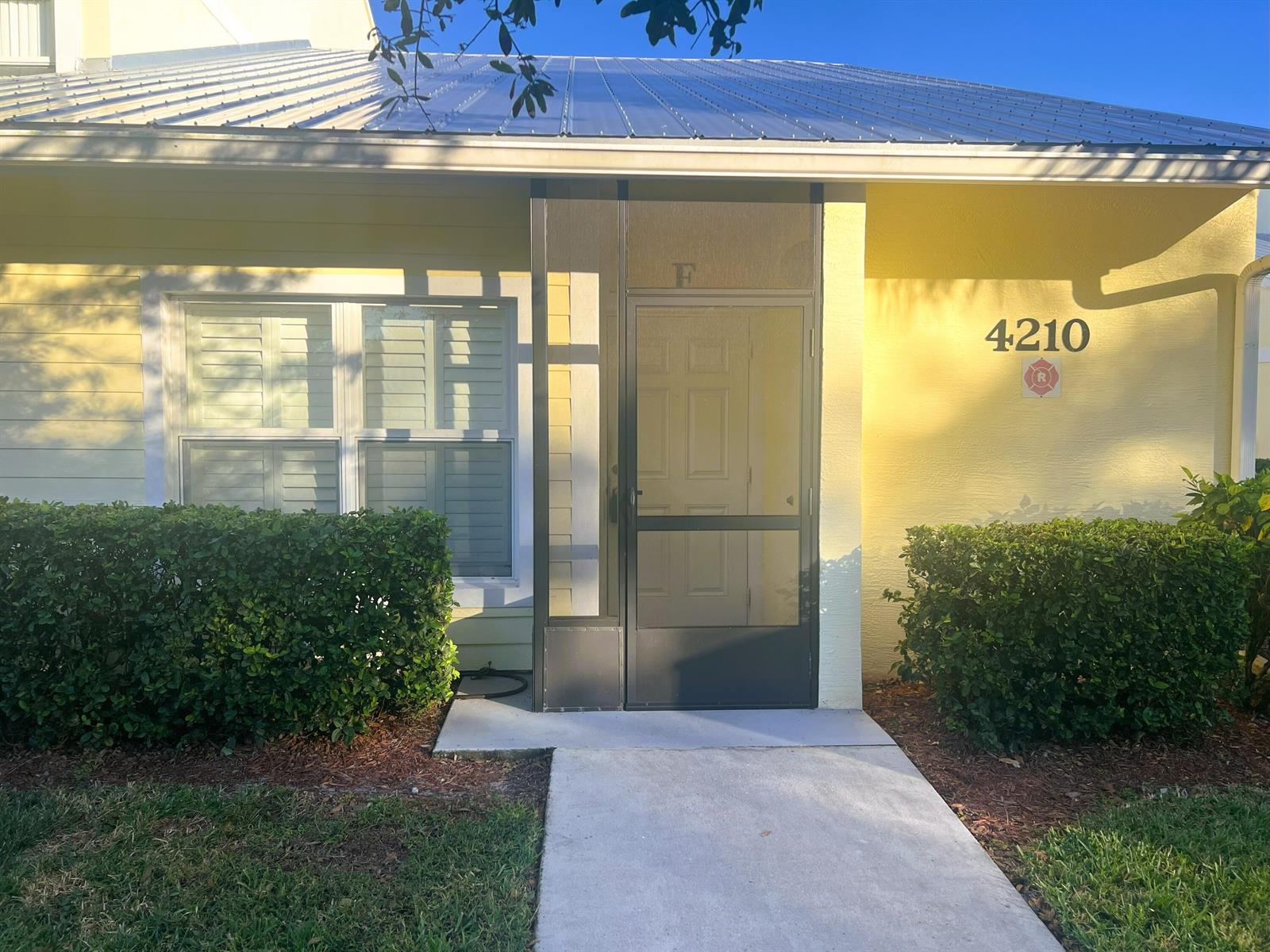 A yellow exterior wall features a screen door, a window with shutters, and house number 4210 — 4210 Gator Trace Circle, Fort Pierce FL 34982, FORT PIERCE, FL