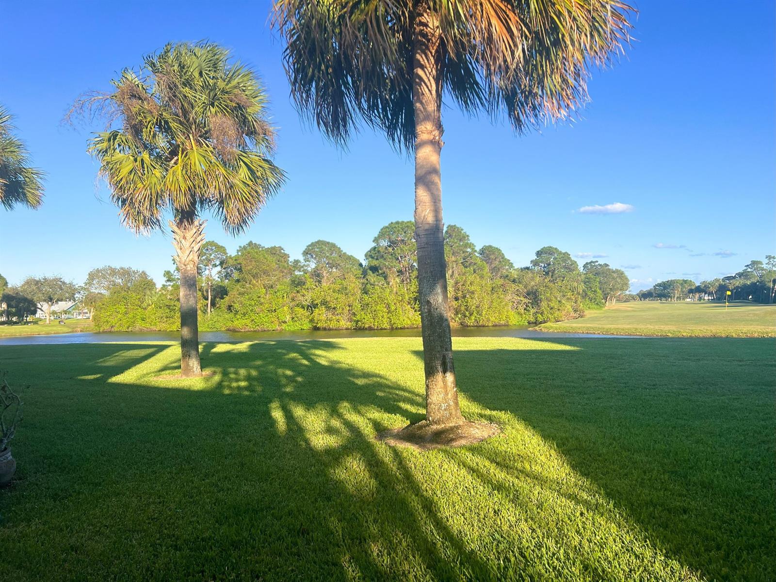 Two palm trees stand on a grassy lawn overlooking a pond and a golf course — 4210 Gator Trace Circle, Fort Pierce FL 34982, FORT PIERCE, FL