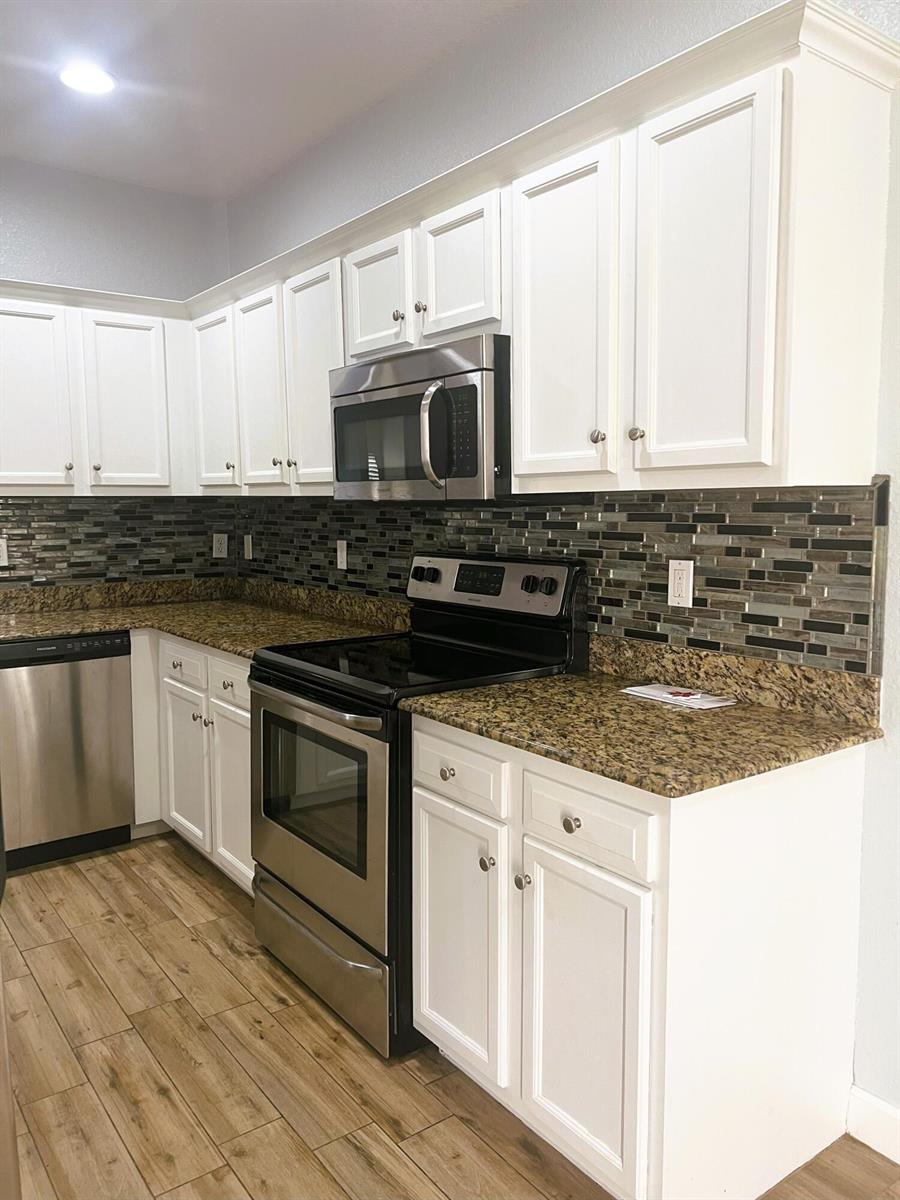 A kitchen features white cabinets, granite countertops, stainless steel appliances, and a glass tile backsplash — 4210 Gator Trace Circle, Fort Pierce FL 34982, FORT PIERCE, FL