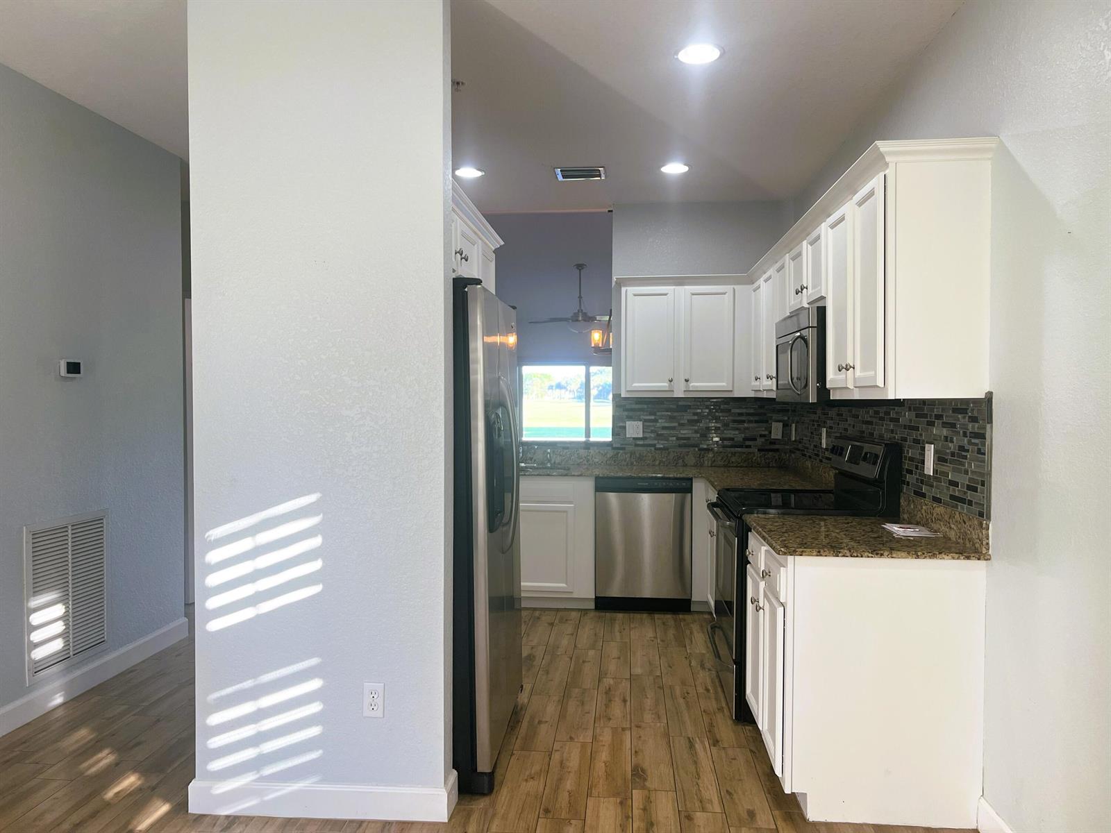 A kitchen with white cabinets, granite countertops, stainless steel appliances, and wood-look tile flooring — 4210 Gator Trace Circle, Fort Pierce FL 34982, FORT PIERCE, FL