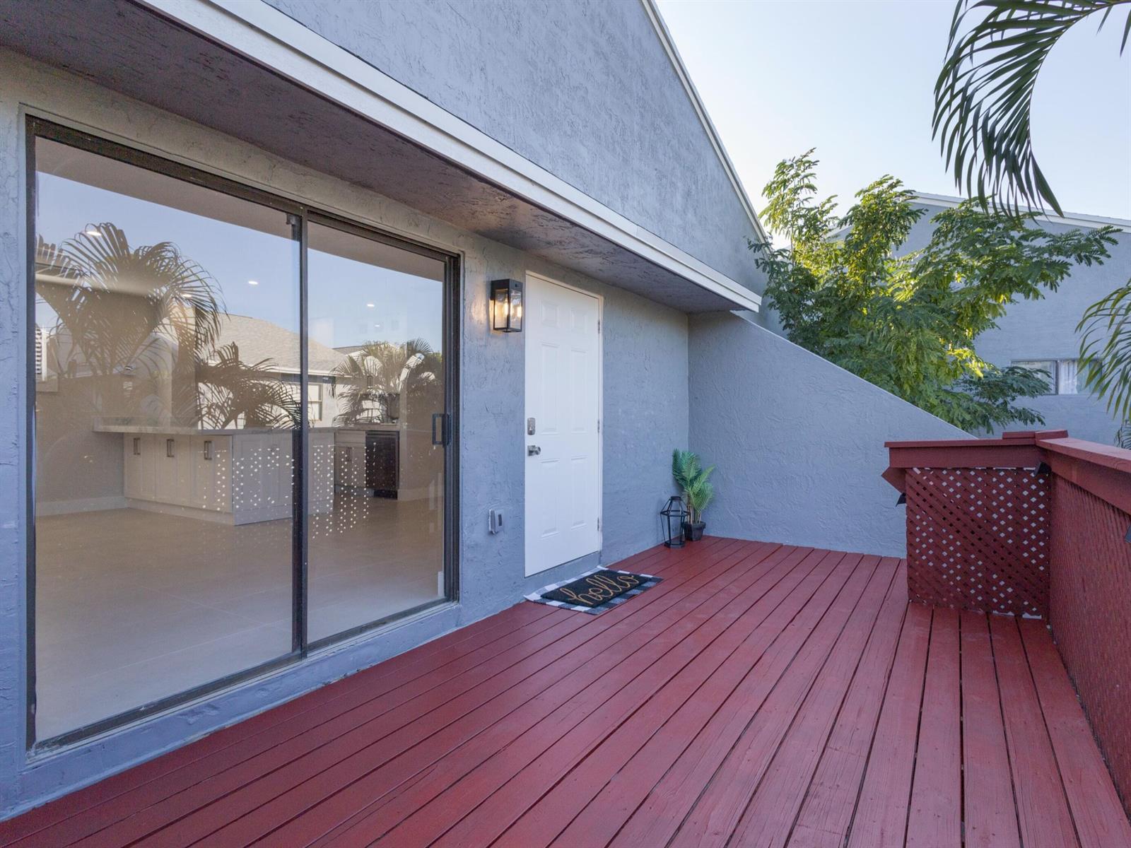 A red wooden deck features a sliding glass door, a white door, and exterior lighting — 7 Crossings Circle # H, Boynton Beach FL 33435, BOYNTON BEACH, FL