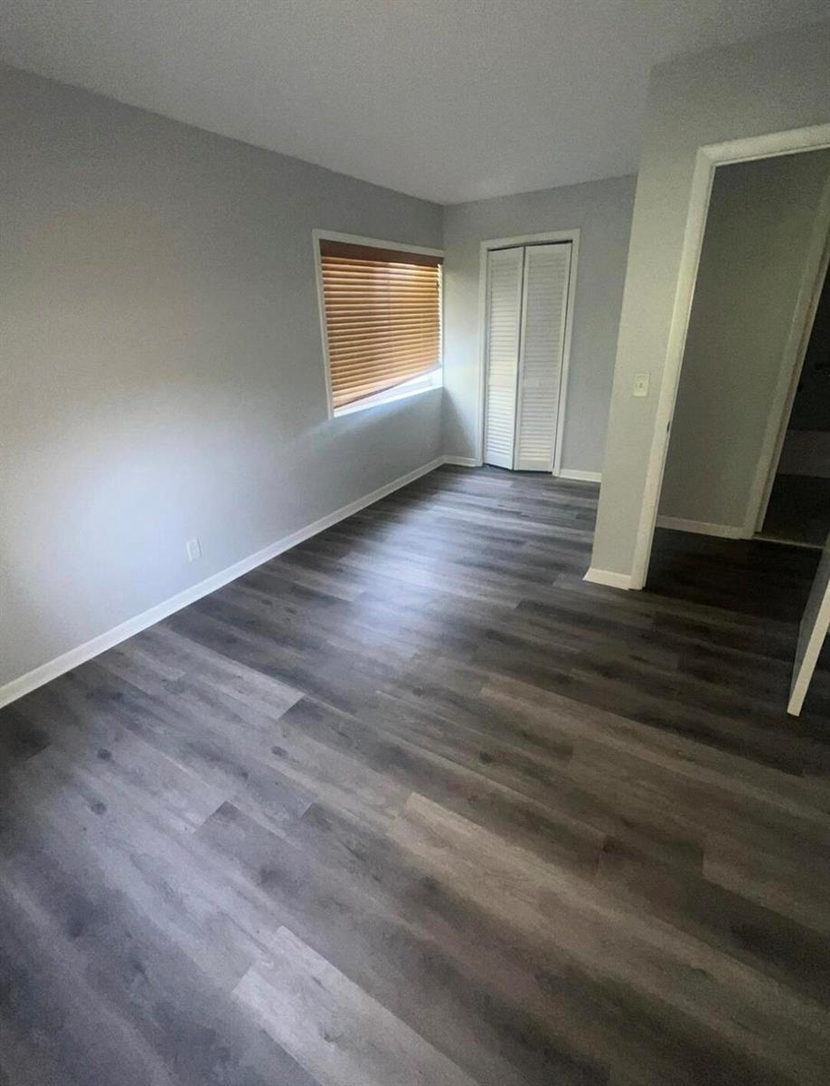 An empty room with light gray walls, dark wood-look flooring, and a white closet — 4815 Sable Pine Circle # C1, West Palm Beach FL 33417, WEST PALM BEACH, FL