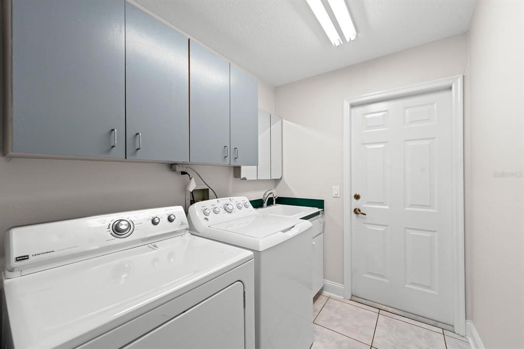 A laundry room features white appliances, gray cabinets, a utility sink, and a white door — 9147 DUFFER COURT, HUDSON, FL