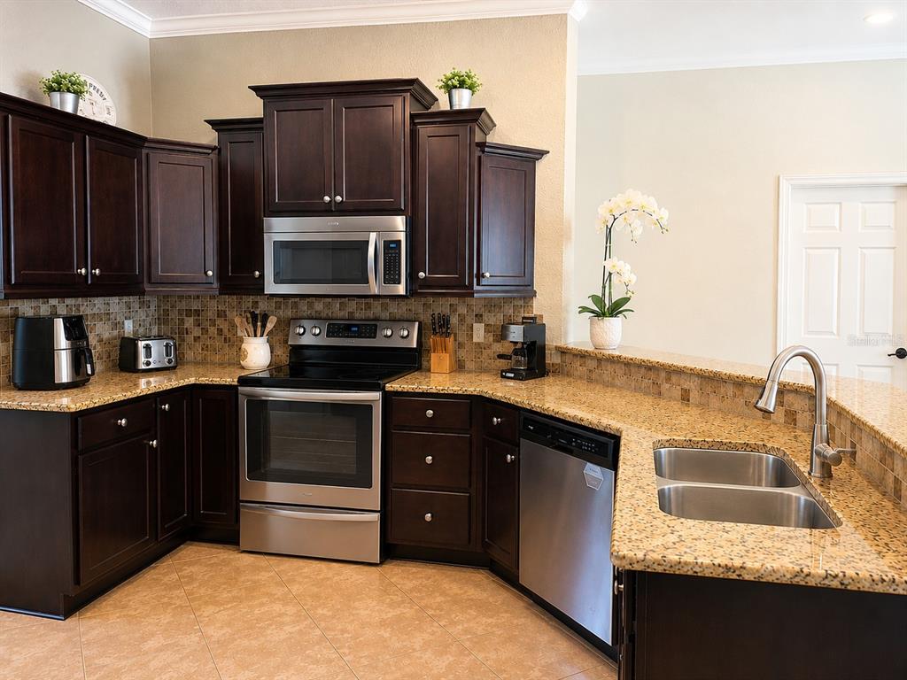 A kitchen features dark wood cabinets, granite countertops, stainless steel appliances, and tile flooring — 4535 SE 34TH PLACE, OCALA, FL