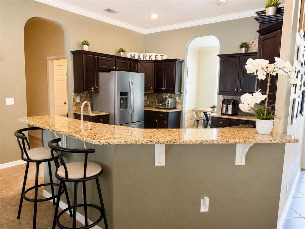 A kitchen features dark wood cabinets, granite countertops, a breakfast bar, and two bar stools — 4535 SE 34TH PLACE, OCALA, FL