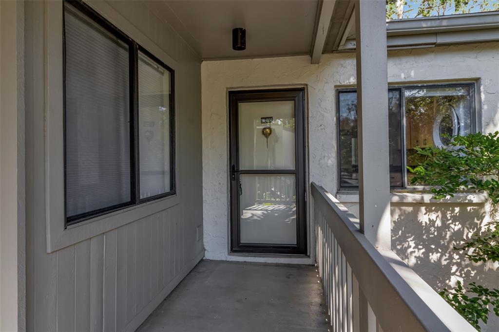 A covered entryway features a glass storm door, gray siding, and a white railing — 1508 PELICAN COVE ROAD UNIT 231, SARASOTA, FL
