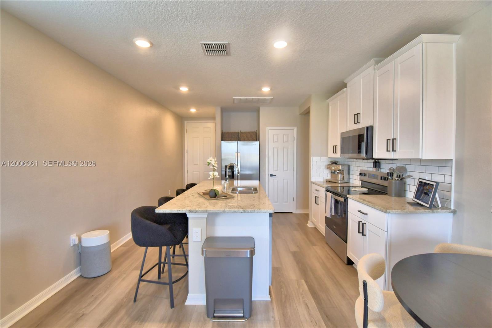 A kitchen features white cabinets, granite countertops, a central island with bar seating, and flooring — 3563 Broadwing Blvd., Kissimmee FL 34759, KISSIMMEE, FL