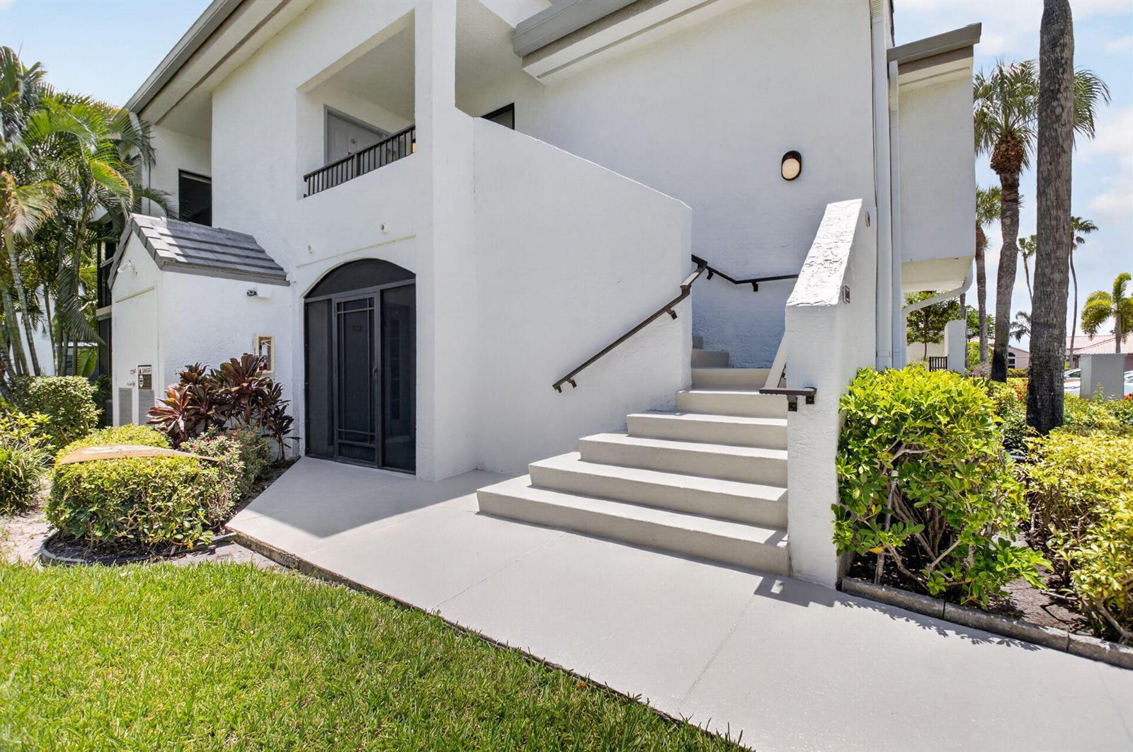 An exterior view of a white two-story building with a concrete staircase and landscaping — 7665 Glendevon Lane # 1605, Delray Beach FL 33446, DELRAY BEACH, FL