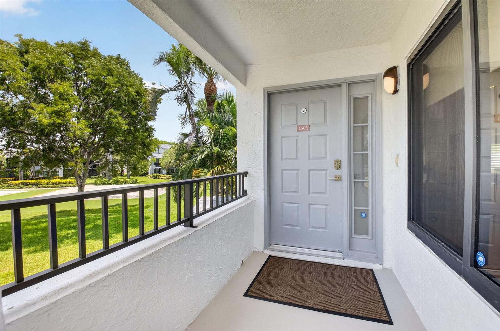 A gray front door with a side window and a doormat on a covered balcony — 7665 Glendevon Lane # 1605, Delray Beach FL 33446, DELRAY BEACH, FL