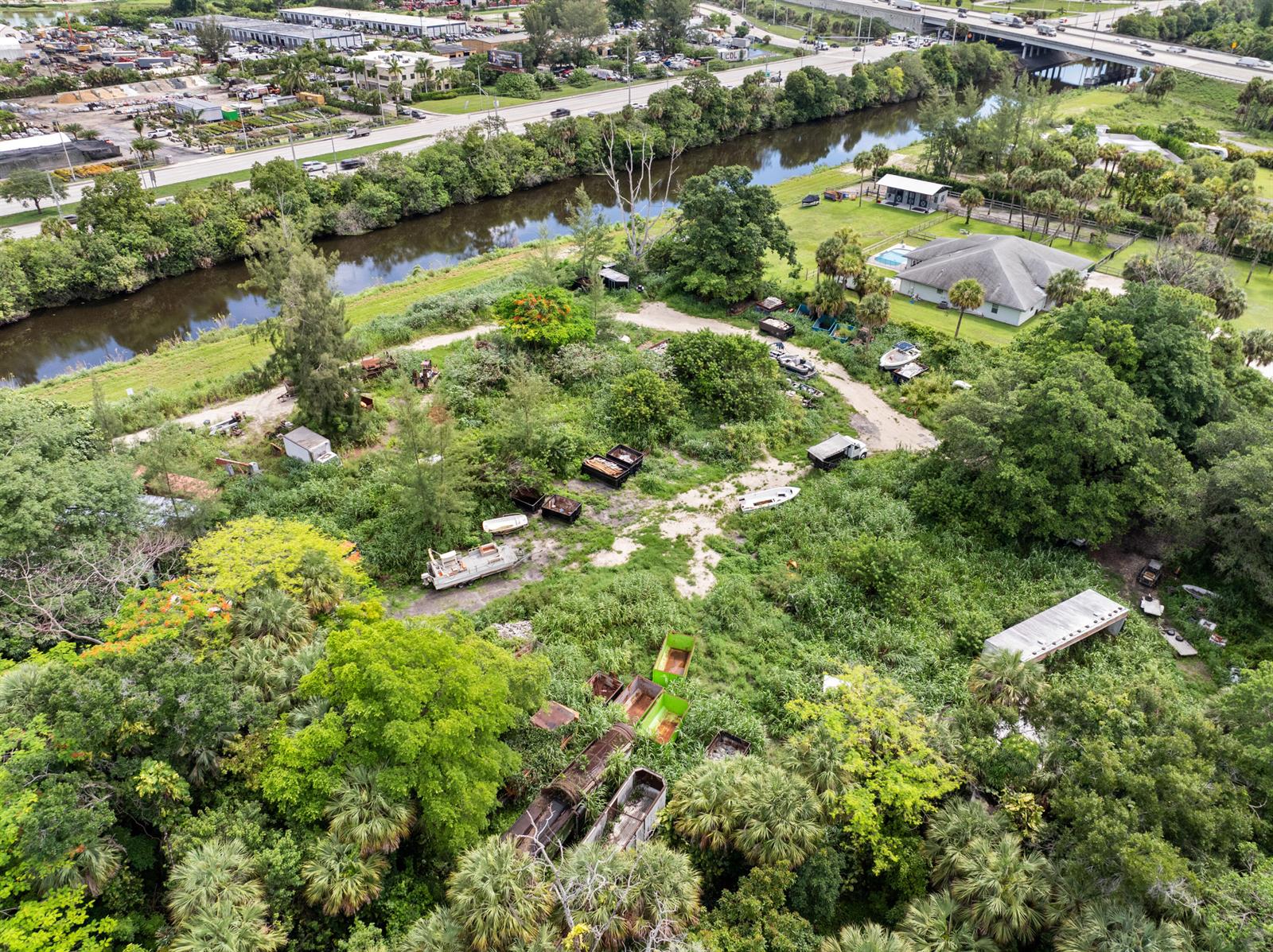 An aerial view shows a wooded lot with scattered debris, dumpsters, and a nearby house — 69 Armadillo Way, West Palm Beach FL 33411, WEST PALM BEACH, FL