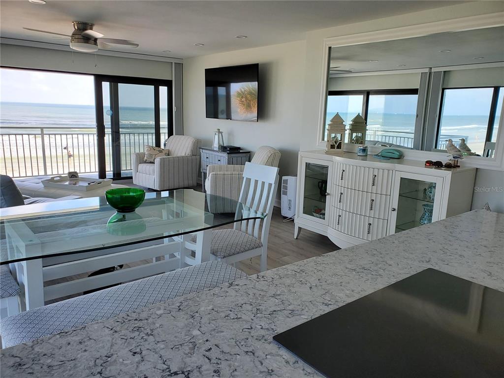 A dining and living area features a glass table, white furniture, and ocean views — 1571 S ATLANTIC AVENUE UNIT 210, NEW SMYRNA BEACH, FL