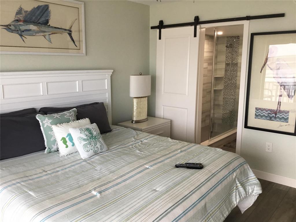 A bedroom features a white headboard, striped bedding, a barn door, and coastal artwork — 1571 S ATLANTIC AVENUE UNIT 210, NEW SMYRNA BEACH, FL