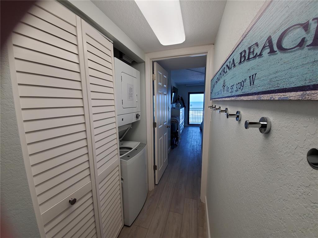 A laundry closet with a stacked washer and dryer sits next to a hallway entrance — 1571 S ATLANTIC AVENUE UNIT 210, NEW SMYRNA BEACH, FL