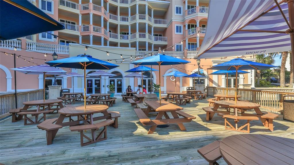 An outdoor patio features multiple picnic tables with umbrellas on a wooden deck — 200 OCEAN CREST DRIVE UNIT 524, PALM COAST, FL