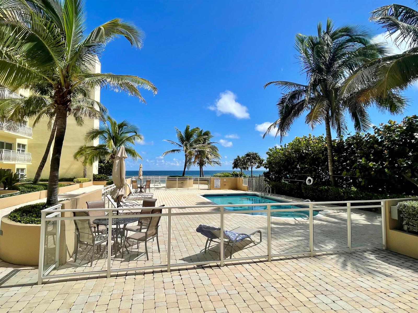 A paved pool deck features lounge chairs, patio tables, and palm trees overlooking the ocean — 310 S Ocean Boulevard # 305, Boca Raton FL 33432, BOCA RATON, FL