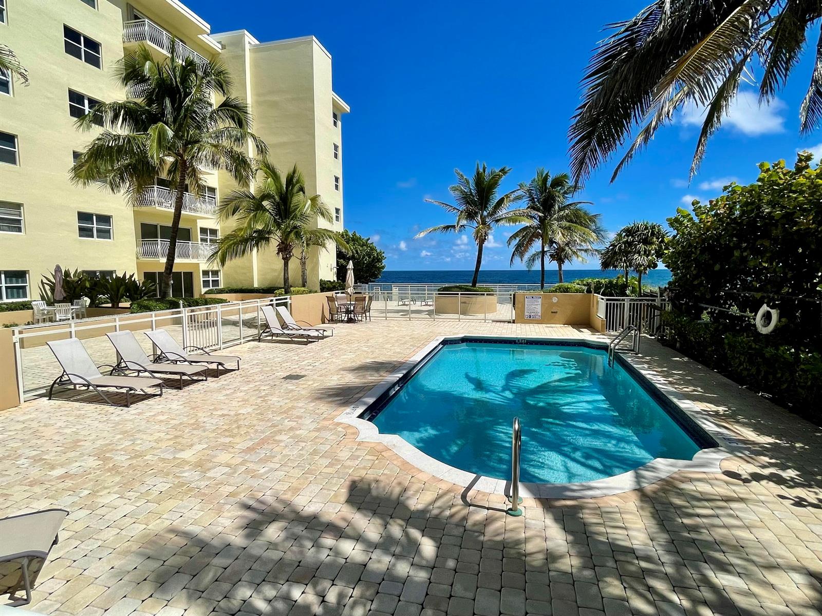 A swimming pool sits on a paved patio next to a multi-story building and ocean — 310 S Ocean Boulevard # 305, Boca Raton FL 33432, BOCA RATON, FL