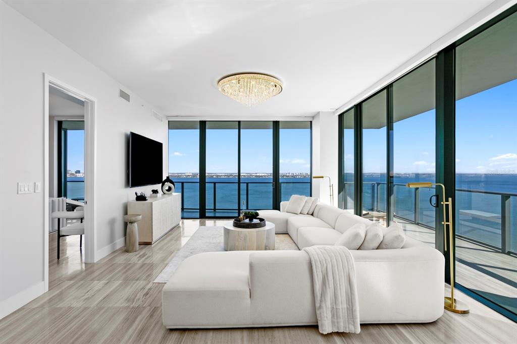 A modern living room features a white sectional sofa, floor-to-ceiling windows, and panoramic water views — 3101 BAYSHORE BOULEVARD UNIT 1804, TAMPA, FL