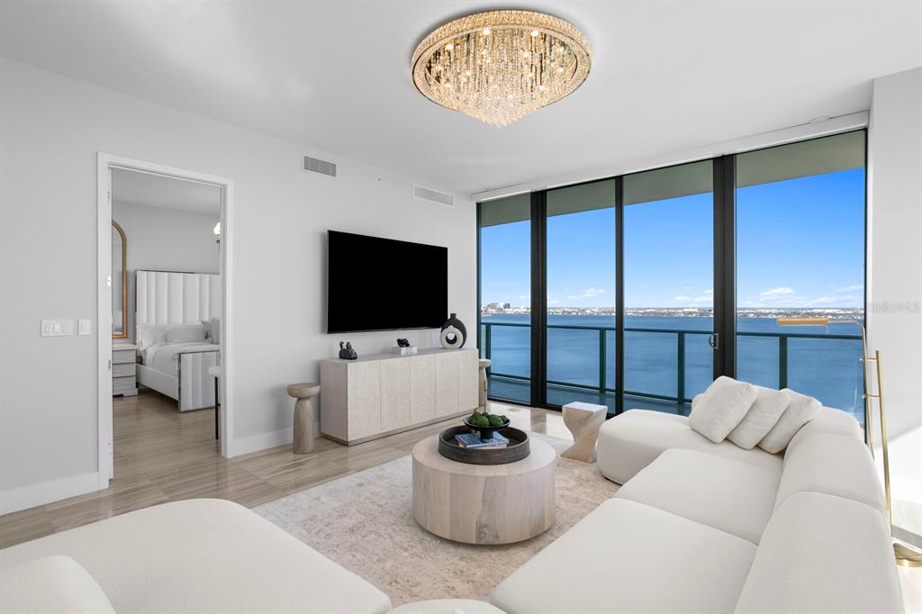 A modern living room features a white sectional, circular coffee table, and floor-to-ceiling waterfront windows — 3101 BAYSHORE BOULEVARD UNIT 1804, TAMPA, FL