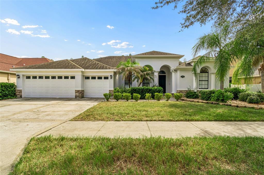 A single-story house with a white stucco exterior, a three-car garage, and a landscaped yard — 19236 CLIMBING ASTER DRIVE, TAMPA, FL