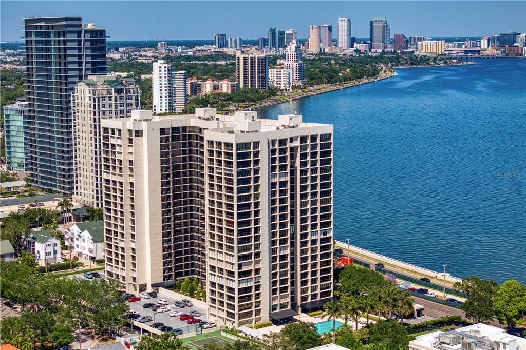 An aerial view shows a tall residential apartment building situated along a waterfront — 3301 BAYSHORE BOULEVARD UNIT 702E, TAMPA, FL