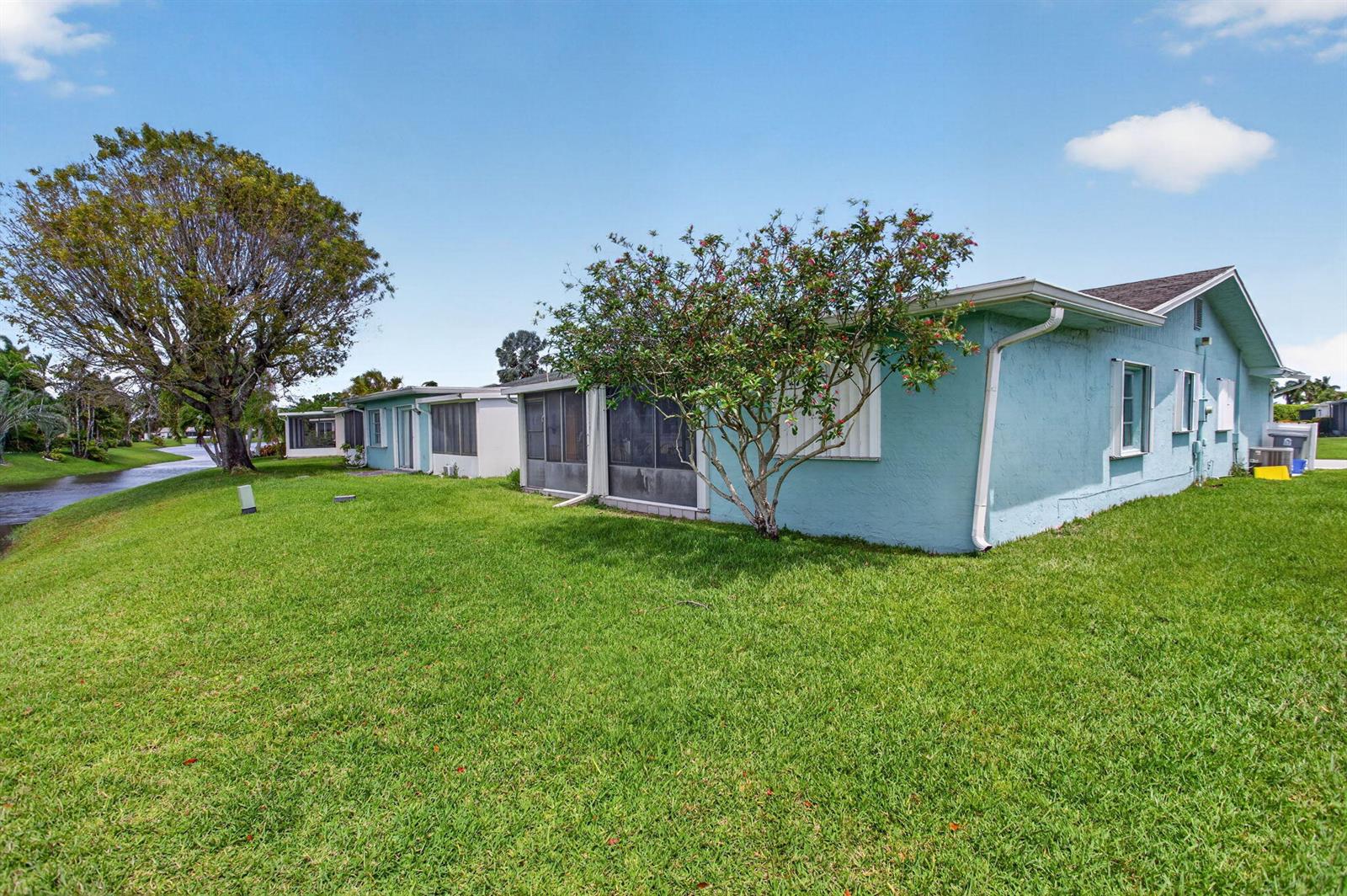 A light blue house with a screened-in porch sits on a grassy lawn near water — 13891 Packard Terrace, Delray Beach FL 33484, DELRAY BEACH, FL