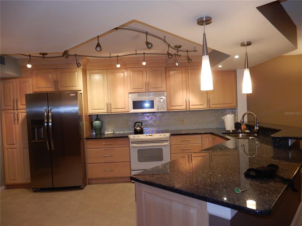 A kitchen with light wood cabinets, dark granite countertops, stainless steel appliances, and track lighting — 5151 ISLA KEY BOULEVARD S UNIT 324, ST PETERSBURG, FL