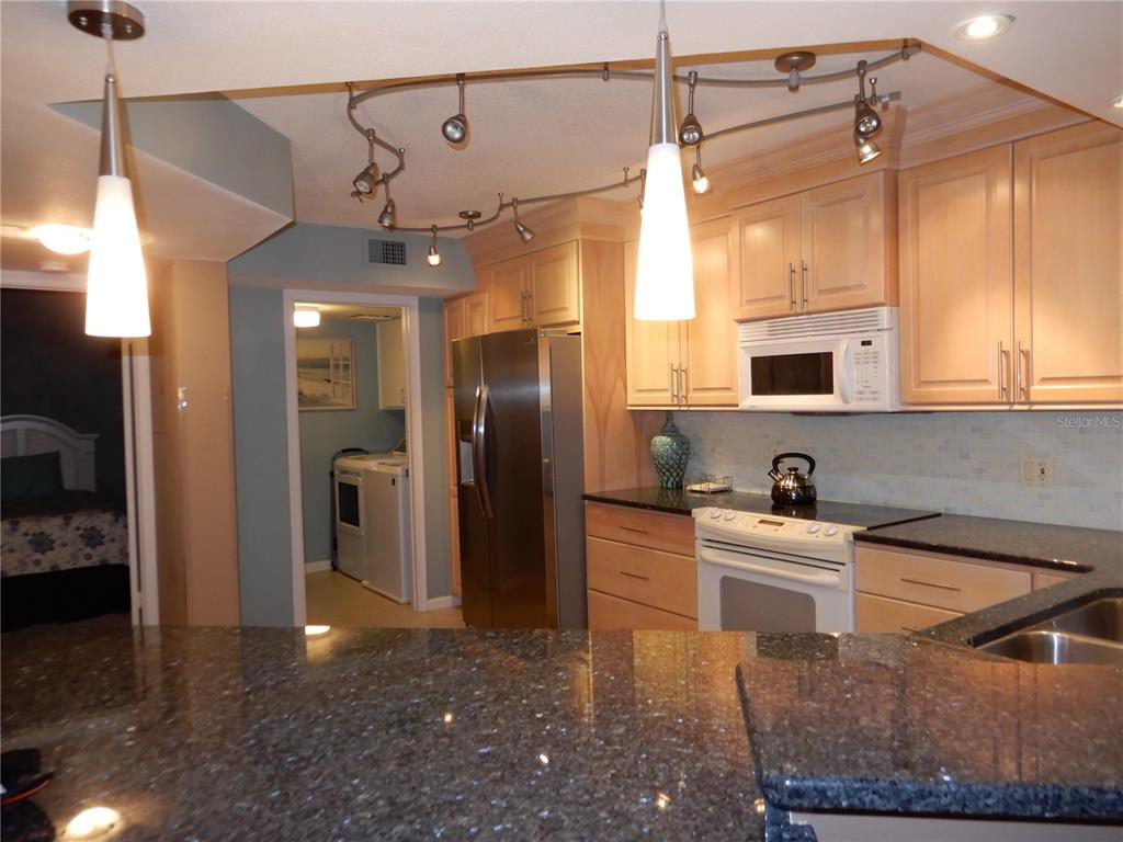 A kitchen features light wood cabinets, dark granite countertops, stainless steel appliances, and track lighting — 5151 ISLA KEY BOULEVARD S UNIT 324, ST PETERSBURG, FL