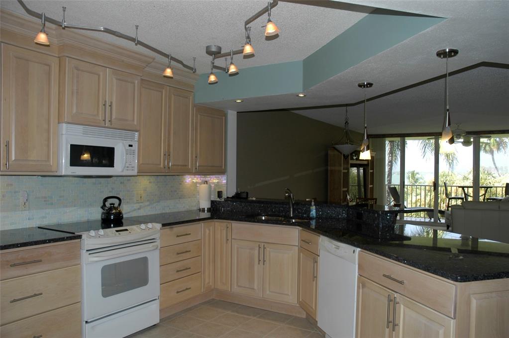 A kitchen features light wood cabinets, dark granite countertops, a white stove, and track lighting — 5151 ISLA KEY BOULEVARD S UNIT 324, ST PETERSBURG, FL