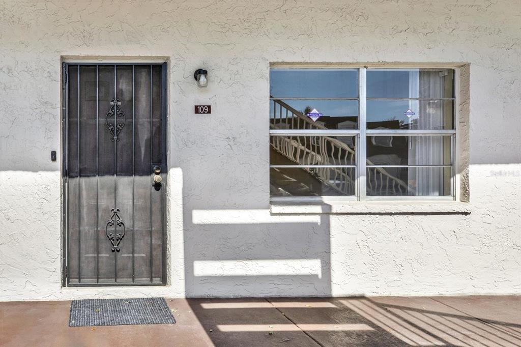 The exterior of a residential unit features a white stucco wall, a security door, and window — 9125 TUDOR DRIVE UNIT D109, TAMPA, FL