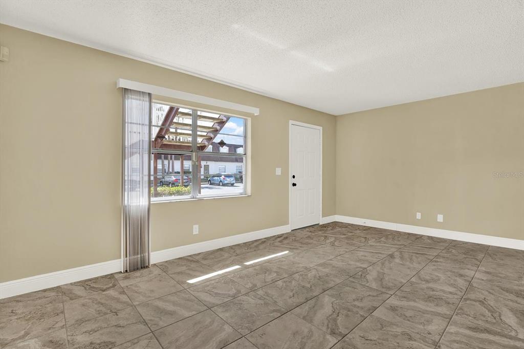 An empty room features tan walls, large gray tile flooring, a window, and a door — 9125 TUDOR DRIVE UNIT D109, TAMPA, FL