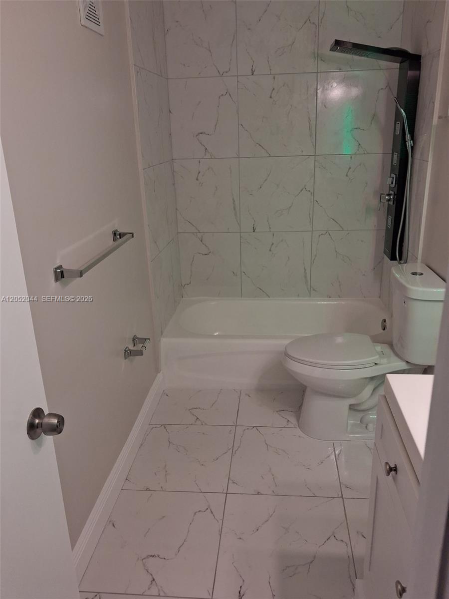 A bathroom features white marble-patterned tile walls and floors, a bathtub, and a toilet — 7245 NW 173rd Dr # 2502, Hialeah FL 33015, HIALEAH, FL