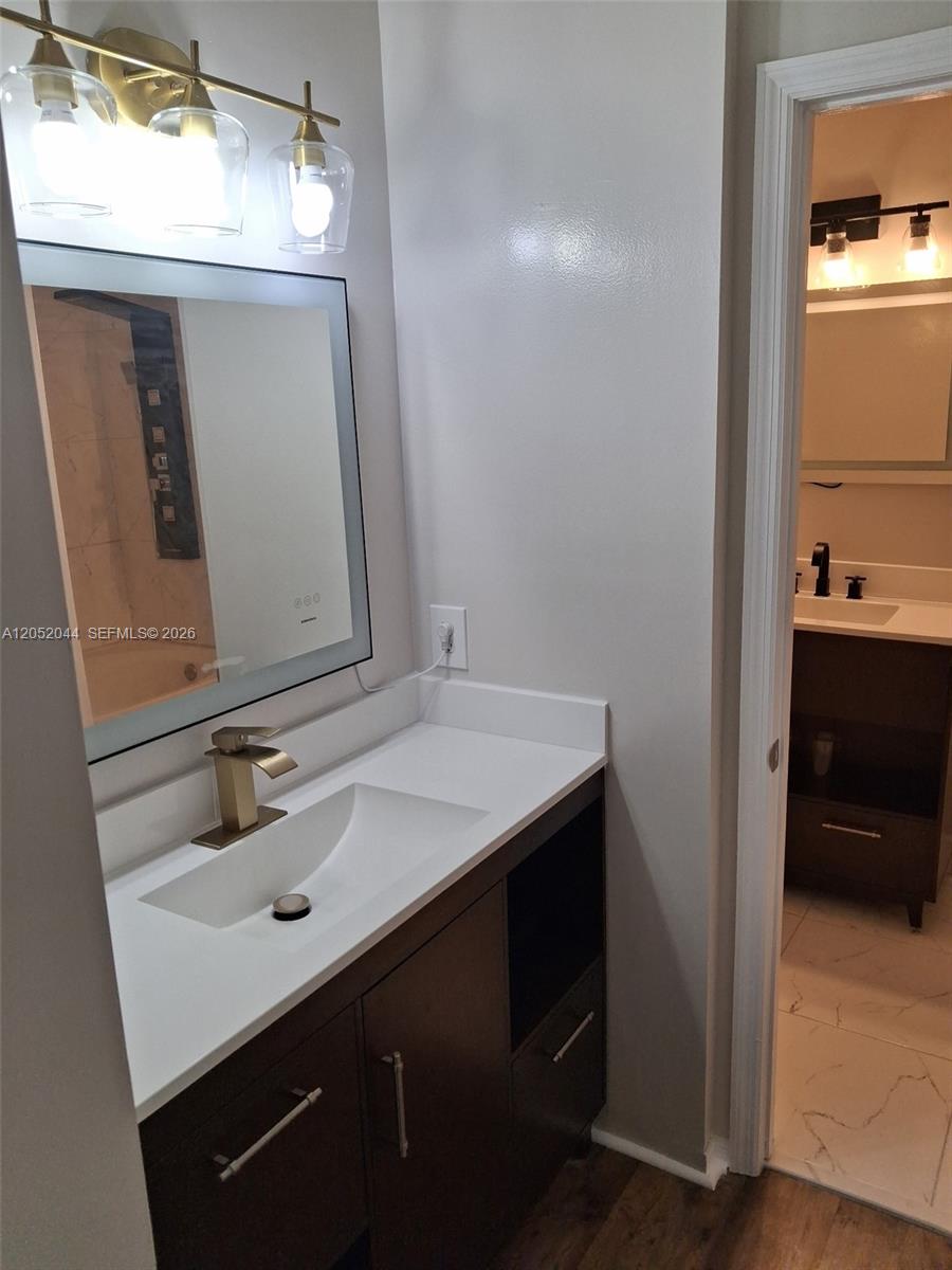 A modern bathroom vanity features a white countertop, gold faucet, and an illuminated mirror — 7245 NW 173rd Dr # 2502, Hialeah FL 33015, HIALEAH, FL