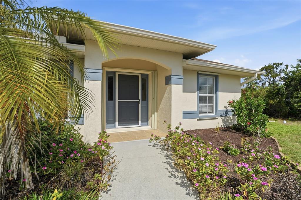 The exterior of a house features a covered entryway, a palm tree, and flower beds — 2291 MEETZE STREET, PORT CHARLOTTE, FL