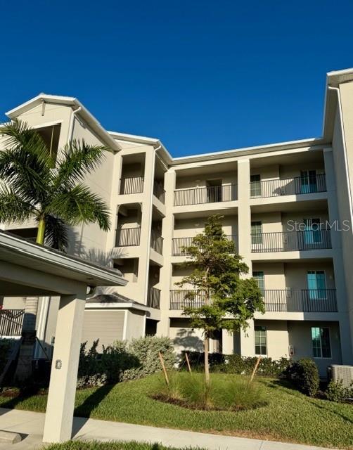 A multi-story apartment building features beige stucco walls, dark metal railings, and a palm tree — 12140 WELLEN GOLF STREET UNIT 402, VENICE, FL