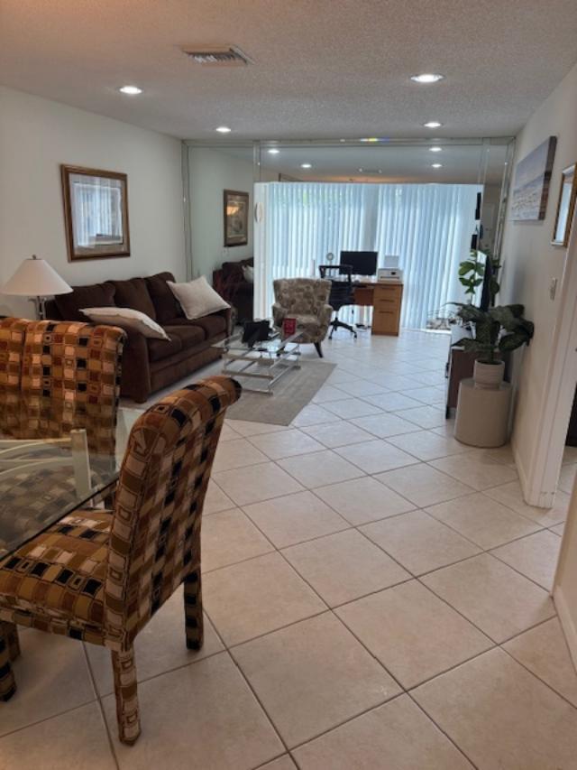 A living room with tile floors, a brown sofa, and a desk near sliding doors — 13678 Vía Flora # B, Delray Beach FL 33484, DELRAY BEACH, FL