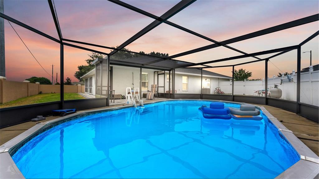 A swimming pool with two floats is enclosed by a screened lanai behind a house — 104 BENTLEY OAKS BOULEVARD, AUBURNDALE, FL