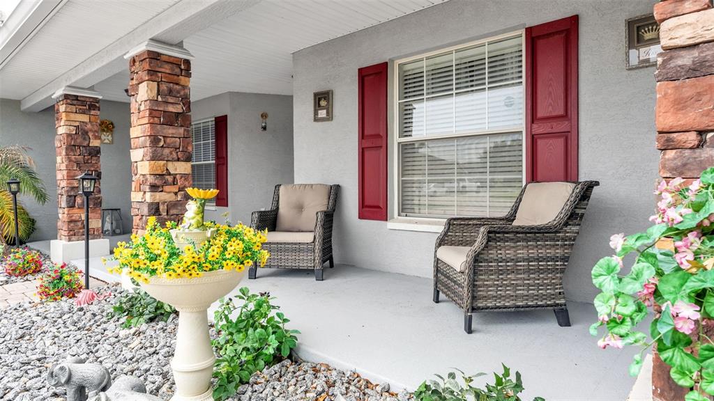 A covered front porch features stone pillars, two wicker chairs, and a decorative flower planter — 104 BENTLEY OAKS BOULEVARD, AUBURNDALE, FL