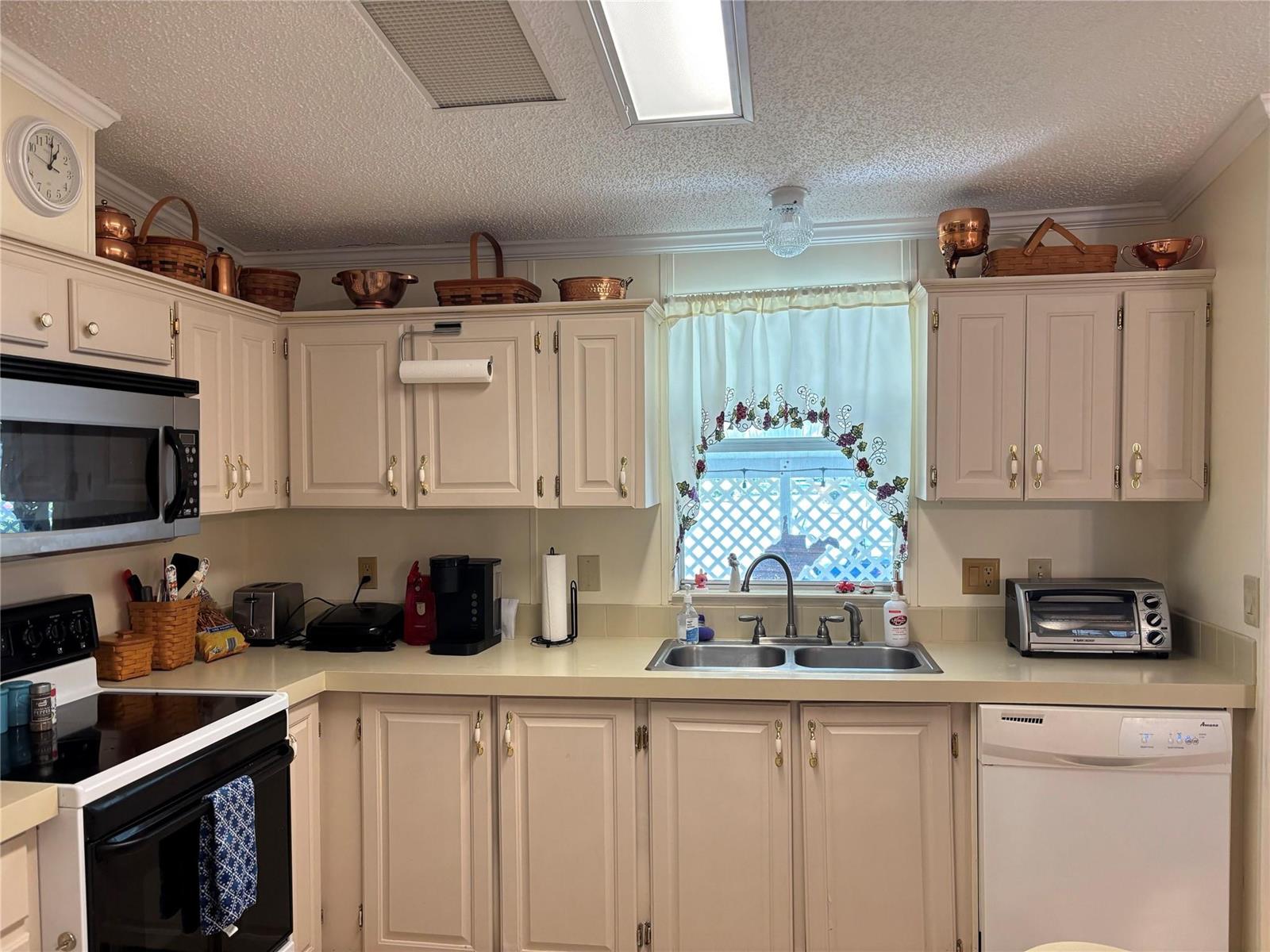 A kitchen features light-colored cabinets, a double sink, a microwave, and decorative baskets on top — 1759 SW 35th Circle, Okeechobee FL 34974, OKEECHOBEE, FL