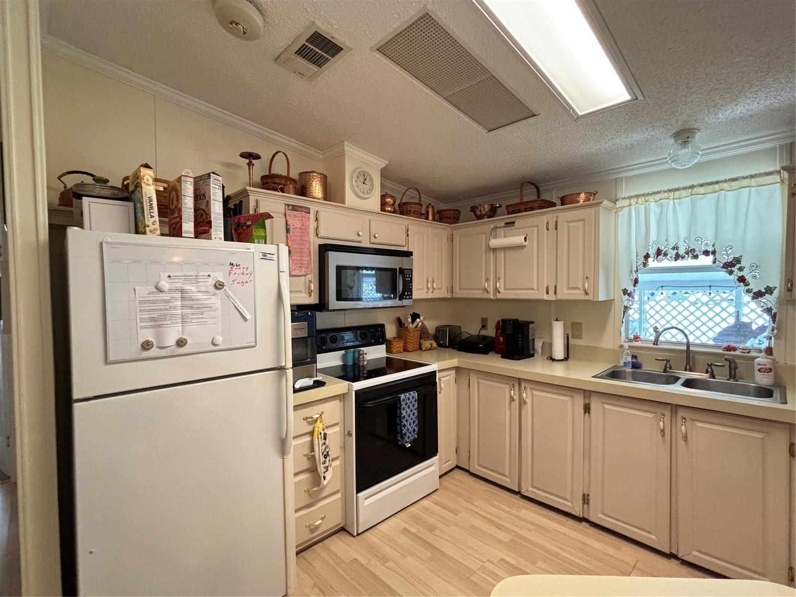 A kitchen with cream-colored cabinets, white appliances, laminate countertops, and a window above the sink — 1759 SW 35th Circle, Okeechobee FL 34974, OKEECHOBEE, FL