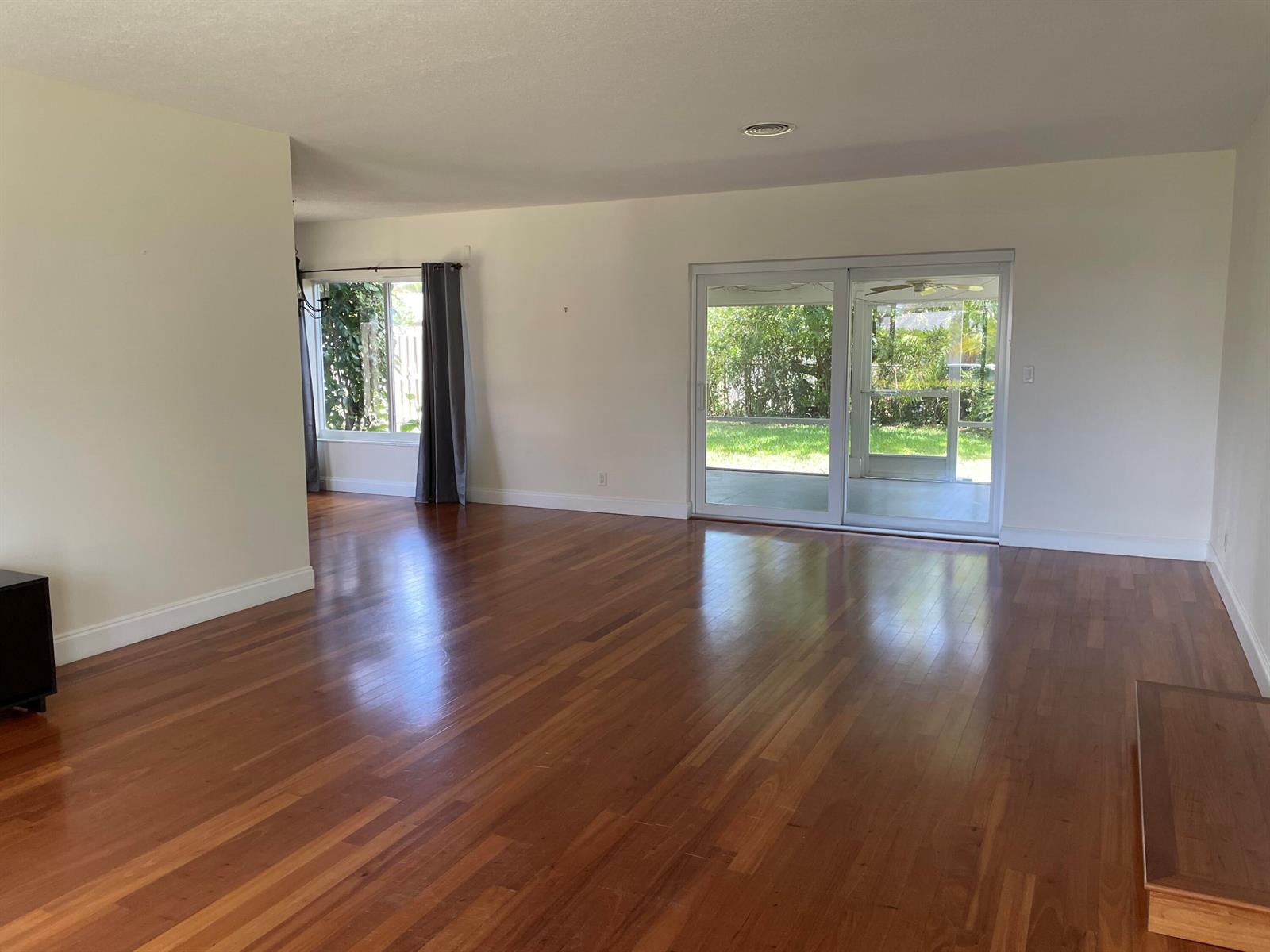 An empty living room features hardwood floors, white walls, and a sliding glass door to a patio — 465 NE 34th Street, Boca Raton FL 33431, BOCA RATON, FL